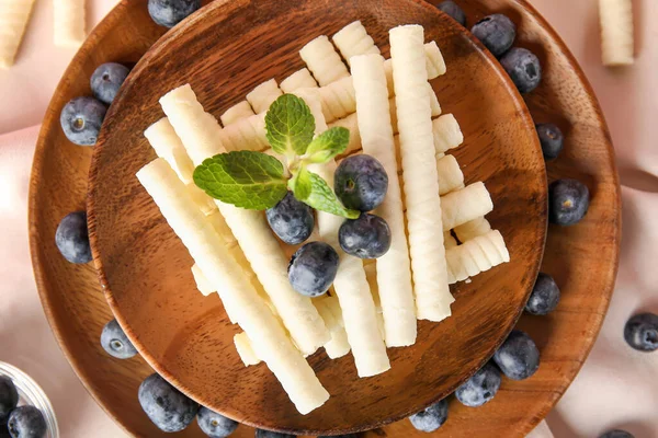 Wooden plates with delicious wafer rolls and blueberries on napkin, closeup