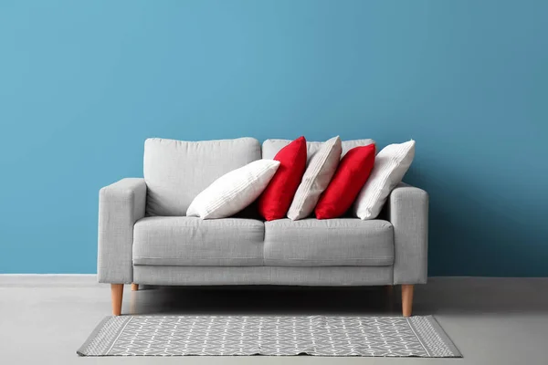 Stylish decorative pillows on cozy grey sofa near blue wall