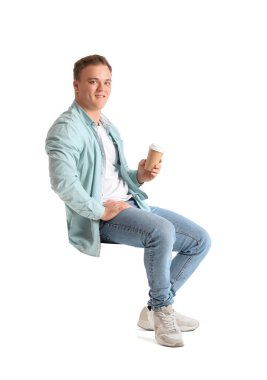 Elinde kahve fincanı olan genç adam beyaz arka planda sandalyede oturuyor.