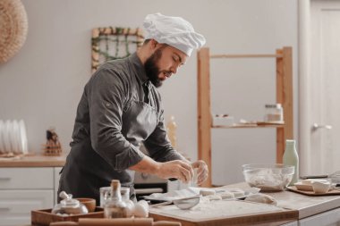 Erkek fırıncı mutfaktaki masada çörek yapıyor.