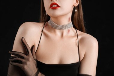 Güzel, genç bir kadın, boynunu karanlık arka planda ısırıyor, yakın plan.