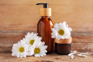 Ahşap arka planda doğal kozmetik ürünleri ve papatya çiçekleri
