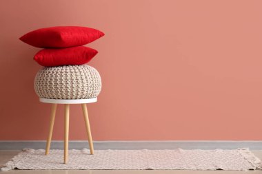 Bir yığın şık dekoratif yastık ve pembe duvarın yanındaki taburede puf.