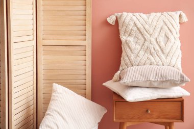 Pembe duvarın yanındaki çekmecede şık dekoratif yastıklar.