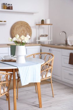 Mutfaktaki yemek masasında ranunculus çiçekleri olan vazo.