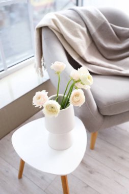 Odadaki koltuğun yanındaki masada ranunculus çiçekli vazo, yakın plan.