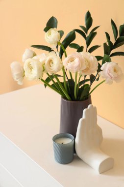 Vase with ranunculus flowers and decor on chest of drawers near beige wall