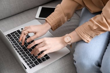 Kol saati olan bir kadın kanepede dizüstü bilgisayar kullanıyor.