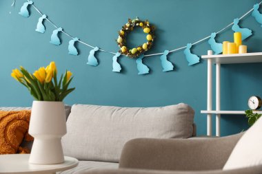 Interior of living room with Easter wreath, paper rabbits and sofa