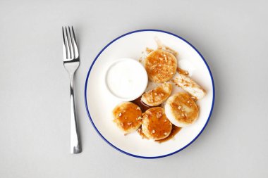 Açık arkaplanda ekşi kremalı bir tabak lezzetli süzme peynirli krep.