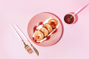 Bir tabak lezzetli süzme peynirli krep, ahududu reçeli ve pembe arka planda ekşi krema.