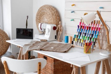 Atölyede iplik makaraları, dikiş makinesi ve dizüstü bilgisayarı olan terzinin işyeri