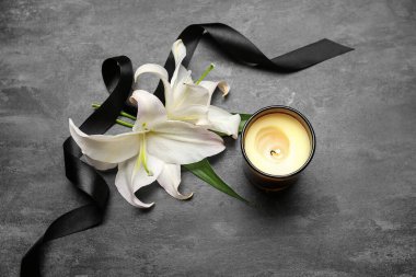 Yanan mum, beyaz zambak çiçekleri ve koyu arkaplanda siyah cenaze kurdelesi olan kompozisyon