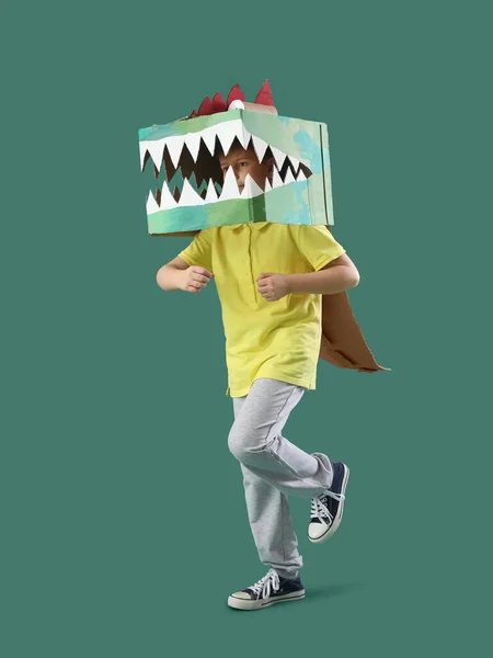 Little boy in cardboard dinosaur costume on green background