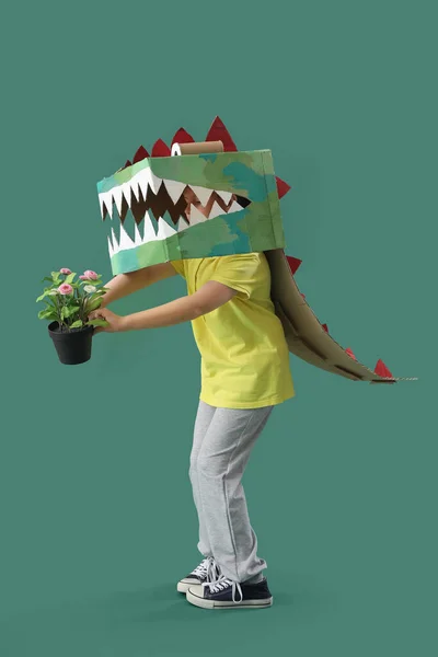 Little boy in cardboard dinosaur costume with flowers on green background