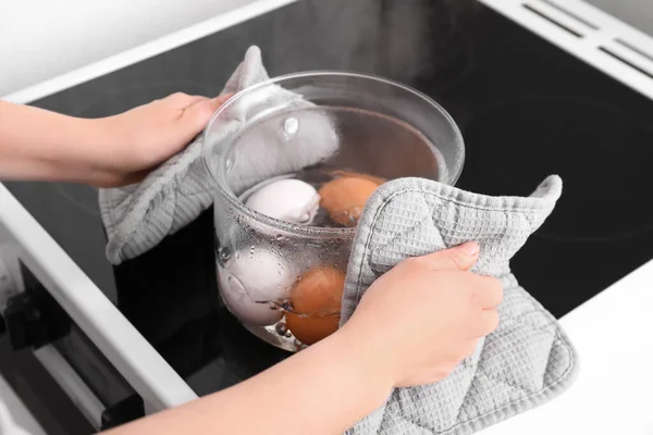 Woman boiling eggs in glass cooking pot on stove, closeup