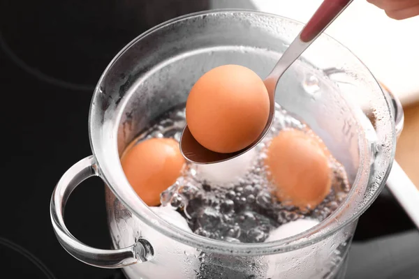 stock image Woman holding spoon with boiled egg above cooking pot on stove, closeup