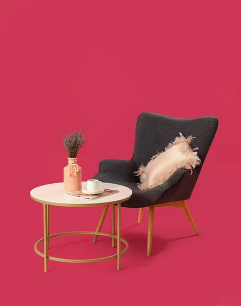 stock image Table with lavender flowers in vase, coffee cup and armchair on pink background