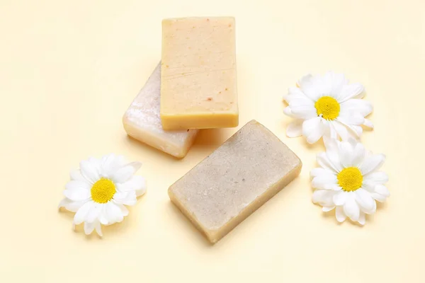 Soap bars and chamomile flowers on color background