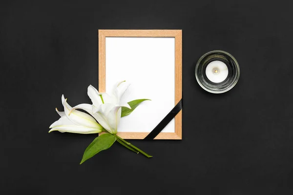 Blank funeral frame, lily flowers and burning candle on dark background