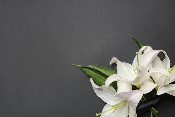 White lily flowers and black funeral ribbon on dark background