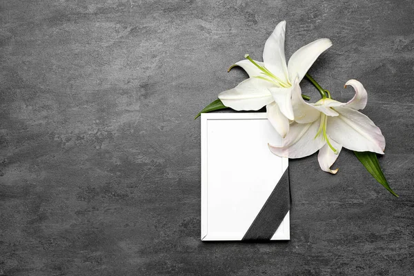 Blank funeral frame and white lily flowers on dark background