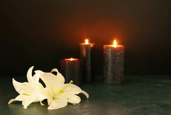 White lily flowers and burning candles on dark table