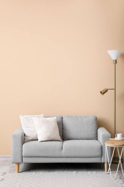 Yastıklı gri kanepe, lamba ve bej duvarlı masa.