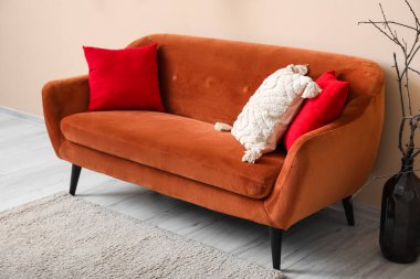 Kahverengi kanepe, bej duvarın yanında yastıklar ve dallar var.