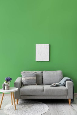 Yastıklı gri kanepe, ekoseli vazo ve yeşil duvarın yanındaki masada sümbül çiçekleri