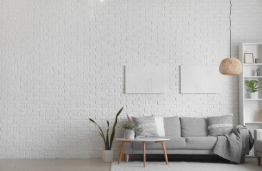 Beyaz tuğla duvarın yanında yastıklı, masalı ve çiçekli gri kanepe.