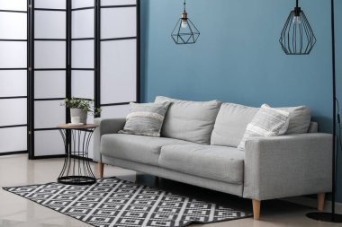 Oturma odasındaki yastıklı, lambalı ve çiçekli gri kanepe.