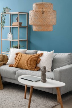 Oturma odasındaki masada yastıklı ve modern laptoplu gri kanepe.