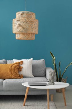 Mavi duvarın yanındaki masada yastıklı ve modern laptoplu gri kanepe.