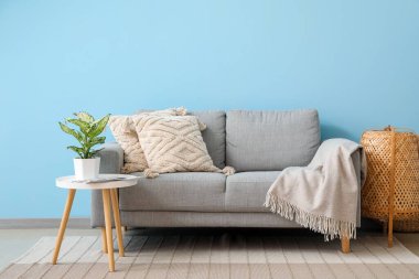 Mavi duvarın yanında, yastıklı ve çiçekli gri kanepe.