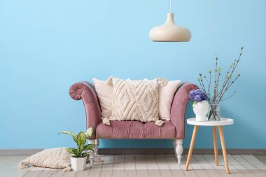 Mavi duvarın yanında yastıklı, masalı ve farklı bitkilerden oluşan rahat bir kanepe.