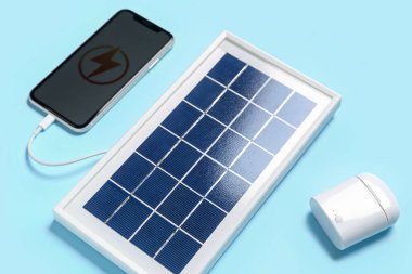 Portable solar panel with mobile phone and earphones on blue background