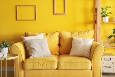 Sarı kanepeli ve çerçeveli oturma odasının içi.