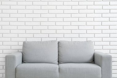 Stylish grey sofa near white brick wall