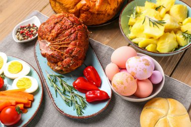 Tasty dishes and painted eggs for Easter dinner on wooden table