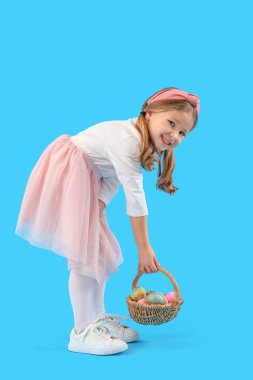 Cute little girl with basket of Easter eggs on blue background