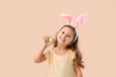 Bej arka planda Paskalya yumurtası olan tavşan kulaklı şirin bir kız.