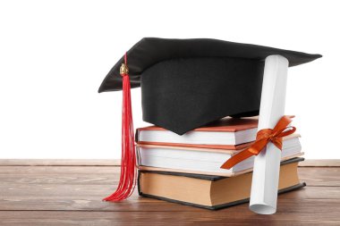 Diplomalı mezuniyet şapkası ve beyaz arka plana karşı ahşap masa üzerindeki kitaplar.