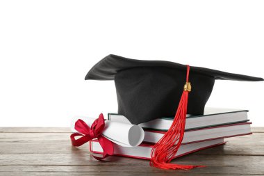 Diplomalı mezuniyet şapkası ve beyaz arka plana karşı ahşap masa üzerindeki kitaplar.