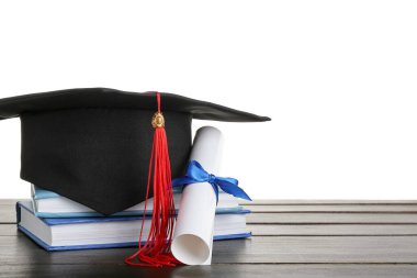 Diplomalı mezuniyet şapkası ve beyaz arka plana karşı koyu ahşap masa üzerine kitaplar.