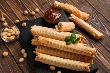 Lezzetli gofret ruloları, kaynamış süt ve kahverengi ahşap arka planda fındıklı fındık.