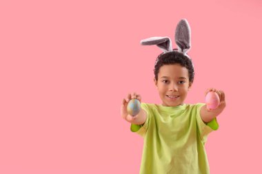 African-American little boy in bunny ears with Easter eggs on pink background