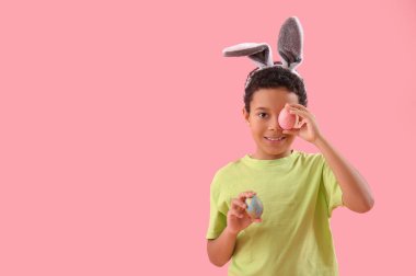 African-American little boy in bunny ears with Easter eggs on pink background