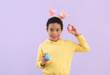 African-American little boy in bunny ears with Easter eggs on lilac background