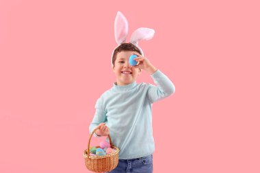 Cute little boy with bunny ears and Easter basket on pink background